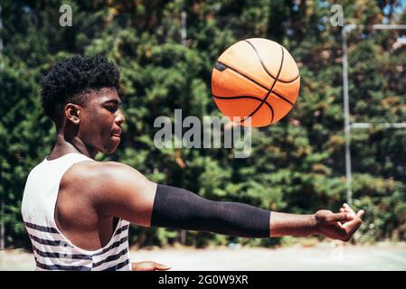 Seitenansicht eines schwarzen afroamerikanischen Jungen, der mit einem Basketball auf einem städtischen Platz Basketball spielt. Stockfoto