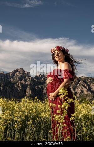 39-jährige schwanger Mädchen in roten Kleid zwischen Feld der gelben Blumen Stockfoto