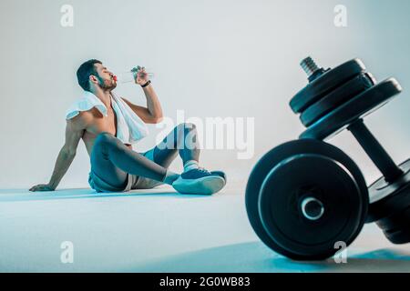 Mann, der Wasser auf dem Hintergrund der Kurzhanteln trinkt Stockfoto