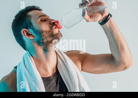 Müder junger Sportler, der Wasser aus der Flasche trinkt Stockfoto