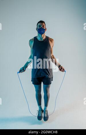 Sportler in medizinischer Maske springen mit Springseil Stockfoto