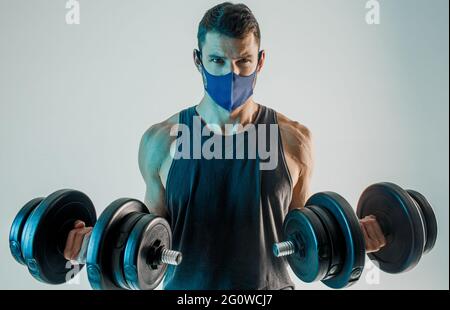 Mann trägt medizinische Maske und Training mit Hanteln Stockfoto