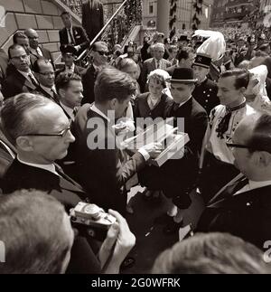 KN-C29294 23. Juni 1963 Präsident John F. Kennedy erhält ein Geschenk, nachdem er während seiner Reise nach Deutschland das Goldene Buch von Köln unterzeichnet hat. Foto: Präsident Kennedy, Fotograf des Weißen Hauses Cecil Stoughton (thront auf einer Treppe), Dolmetscher Robert H. Lochner, Stadtbeamte und Zuschauer. Rathaus, Bonn, Deutschland. Bitte nennen Sie „Robert Knudsen. Fotografien Des Weißen Hauses. John F. Kennedy Presidential Library and Museum, Boston' Stockfoto