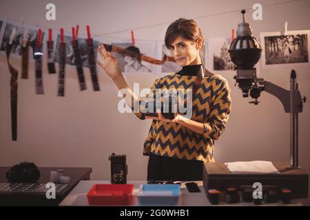 Glückliche junge Frau mit Filmstreifen und lächelnd. Portrait von kreativen Mädchen Fotograf in Fotostudio Dunkelkammer. Entwicklung eines analogen Kamerafilms Stockfoto