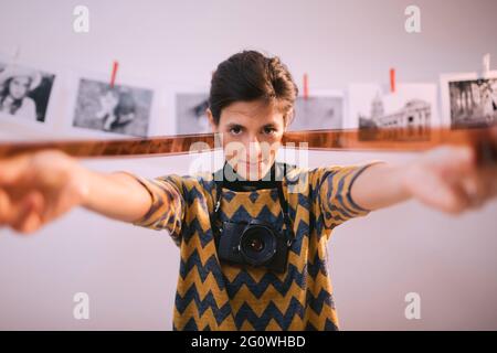 Glückliche junge Frau mit Filmstreifen und lächelnd. Portrait von kreativen Mädchen Fotograf in Fotostudio Dunkelkammer. Entwicklung eines analogen Kamerafilms. Stockfoto