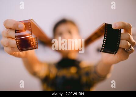 Glückliche junge Frau mit Filmstreifen und lächelnd. Portrait von kreativen Mädchen Fotograf in Fotostudio Dunkelkammer. Entwicklung eines analogen Kamerafilms. Stockfoto