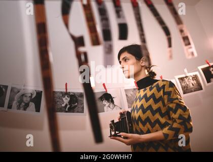 Frau, die mit einer alten Kamera fotografiert. Portrait von kreativen Mädchen Fotograf in Fotostudio Dunkelkammer. Entwicklung eines analogen Kamerafilms Stockfoto