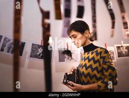 Frau, die mit einer alten Kamera fotografiert. Portrait von kreativen Mädchen Fotograf in Fotostudio Dunkelkammer. Entwicklung eines analogen Kamerafilms Stockfoto