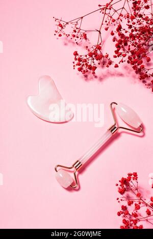 Jade Gesicht Massage Roller und Sha Sha auf rosa Hintergrund. Hautpflege- und Spa-Werkzeuge Stockfoto