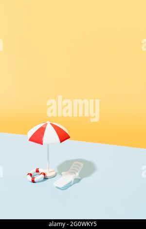 Weißer und roter Sonnenschirm, Sonnenstuhl, blau-weiß gestreiftes Handtuch und Rettungsbojen auf blauem und gelbem Hintergrund. Strandset für sonnige Tage. Sommer h Stockfoto