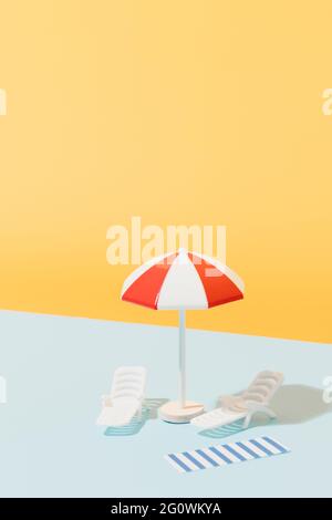 Weißer und roter Sonnenschirm, Liegestühle und blau-weiß gestreiftes Handtuch auf blauem und gelbem Hintergrund. Strandset für sonnige Tage. Sommerurlaub Konz Stockfoto