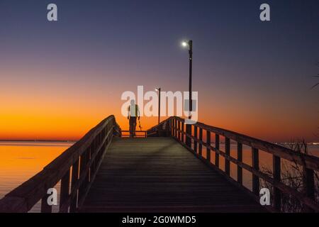 Ein Fischer blickt auf das letzte Leuchten der untergehenden Sonne, während er am 12. November 2020 über den Bayfront Park Pier in Daphne, AL, USA, läuft. Stockfoto