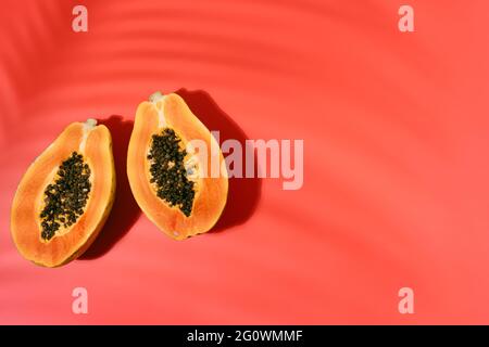 Frische Papaya mit schwarzen Samen auf rotem Hintergrund mit Schatten der Kokosnussblätter im Sommer. Ferien- und Naturkonzept. Kopierraum. Draufsicht Stockfoto