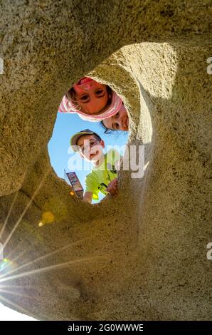 Тhree lächelnde Kinder erscheinen durch ein Loch in einem Felsen. Stockfoto