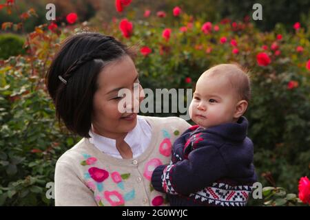 Japanische Mutter hält entzückende Tochter in einem Outdoor Blumengarten. Stockfoto