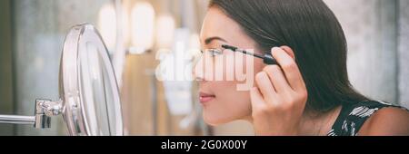 Frau Putting Mascara Make-up in Spiegel Banner immer bereit für die Arbeit tun Morgen Make-up Routine Putting Mascara in Bad Spiegel zu Hause Stockfoto