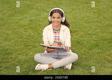 Ideenkonzept. Kinder hören Musik auf grünem Gras. Gesunde Lebensweise und entspannen. Mädchen schreiben Erinnerung in Tagebuch. Kleines Kind in den Kopfhörern. Sommer im Freien Stockfoto