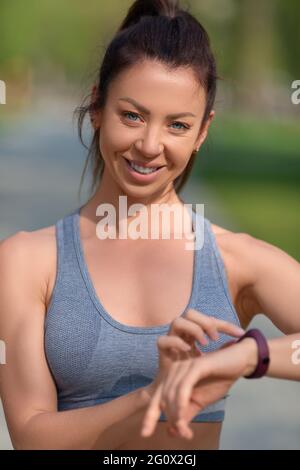 Nahaufnahme einer Frau. Sie lächelt, blickt auf die Kamera und überprüft ihren Puls nach dem Rennen mit ihrer Smartwatch. Das Konzept eines gesunden Lebensstils A Stockfoto