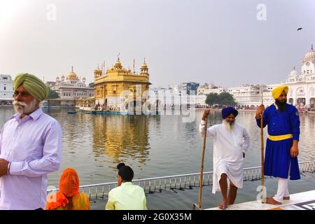 AMRITSAR, INDIEN - 06. November 2016: Weitwinkel des goldenen Tempels und des heiligen Pools in amritsar mit einem Anhänger, der am Teich sitzt, zusammen mit 2 Sikh s Stockfoto