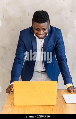 Afroamerikanischer Geschäftsmann in einem modernen Büro vor Verhandlungen oder Treffen Blick auf gelben Laptop auf den Tisch gelehnt für das Treffen vorbereitet Stockfoto