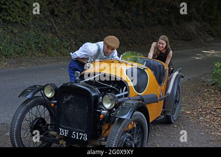 Männer und Frauen schieben auf dem Land den heruntergekommenen Oldtimer auf die Straße.Paar schiebt ihr abgebrochenes Auto. Stockfoto