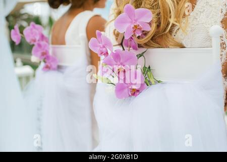 Blumenschmuck auf einem Stuhl mit Orchideen bei einer schwulen Hochzeit zweier Frauen. Nicht erkennbare Person Stockfoto