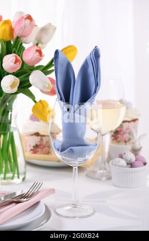 Eine Serviette, die in Form von Hasenohren in einem Glas gefaltet ist, das Konzept, zu Ehren von Ostern einen festlichen Tisch zu legen. Stockfoto