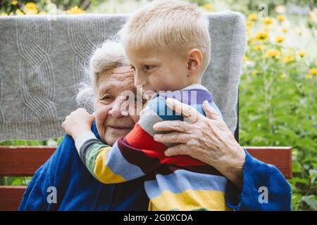 90-jährige ältere Frau Ur-Großmutter umarmt Ur-Enkel. Kind Junge Unterstützung und Blumen zu Ur-Großmutter. Familiengruppe, Unterstützung Stockfoto