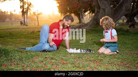 Vater und Sohn spielen Schach auf Gras im Sommerpark, Familie Stockfoto