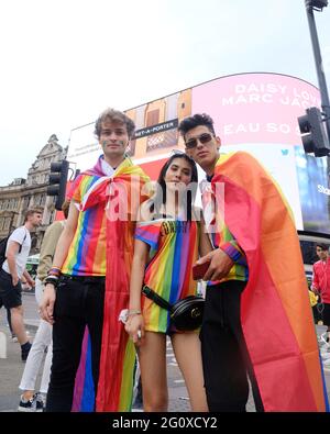 Drei junge Feiernden, die mit Regenbogenfahnen drapiert sind, erfreuen sich an den Feierlichkeiten der Pride in London, als die Veranstaltung 2019 50 Jahre seit dem Stonewall-Aufstand markiert Stockfoto