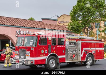 Lompoc, CA, USA - 26. Mai 2021: Nahaufnahme eines roten Feuerwehrmotors in der Stadt mit einem Offizier und vor dem Hilton Garden Inn in der Innenstadt. Stockfoto