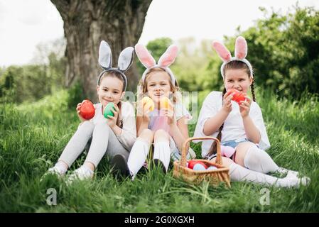 Ostereiersuche. Eine Gruppe von Kindern mit Hasenohren läuft auf der Ostereiersuche im Garten, um bunte Eier abzuholen. Ostertradition Stockfoto