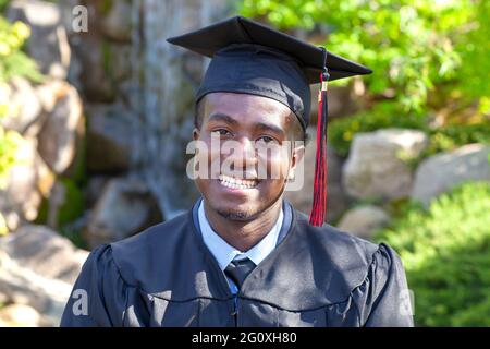 Hübscher junger schwarzer College-Absolvent, der Mütze und Kleid trägt und stolz lächelt Stockfoto