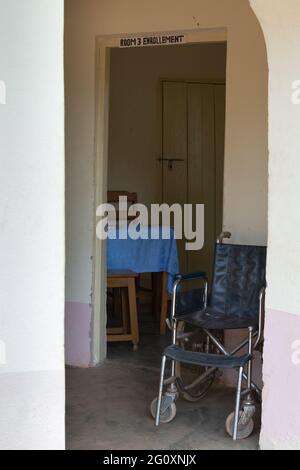 Ein alter, rostiger Rollstuhl im Flur und ein Blick in eine Registrierung sind durch einen Türlosen Eingang zu sehen. Stockfoto