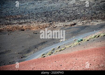Straße, die ein wunderschönes vulkanisches Gebiet auf Lanzarote durchquert. Lavagestein, roter Sand und Kaktus. Kanarische Inseln, Spanien, Europa. Stockfoto