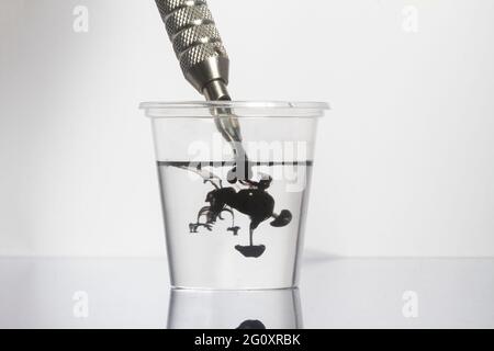 Tattoo Maschine schwarze Tintennadeln mit sauberem Wasser in klarem Glas reinigen Stockfoto