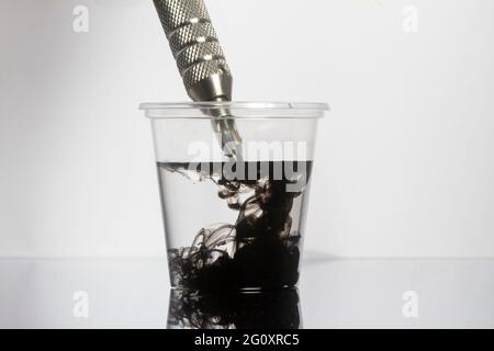 Tattoo Maschine schwarze Tintennadeln mit sauberem Wasser in klarem Glas reinigen Stockfoto