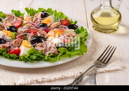 Einfach einen Thunfischsalat auf einem weißen Teller gekocht und über einem Holztisch gabelt. Mediterraner Thunfischsalat mit Eiern und Gemüse. Kalorienarme gesunde Ernährung. Stockfoto