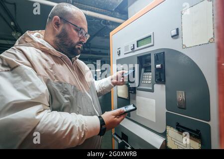 Der Mann zahlt für die Tiefgarage im automatischen Zahlungsterminal eines Einkaufszentrums mit seinem Telefon oder seiner Karte. Stockfoto