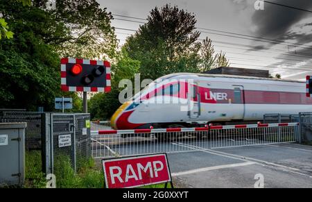 Der elektrifizierte Hochgeschwindigkeitszug Azuma führt an einem auotmatischen unbemannten Bahnübergang auf der Hauptlinie der Ostküste vorbei. Stockfoto