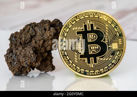 Bitcoin-Token aus Gold mit einem vulkanischen Gestein, das den Abbauprozess symbolisiert Stockfoto