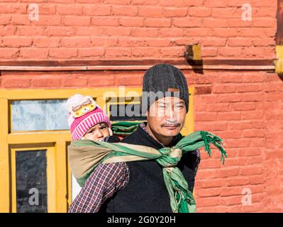 Porträt eines Mannes, der sein Baby während des Winterschneehaltens in himachal pradesh auf dem Rücken trägt. Stockfoto