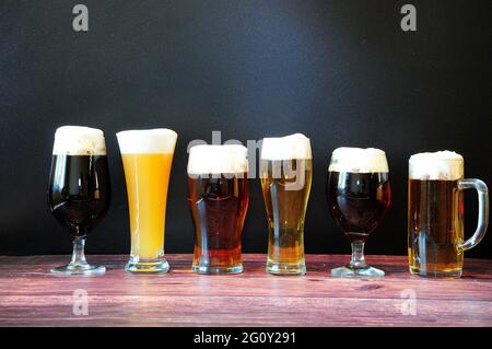 Auf einem Holztisch stehen sechs Gläser verschiedener Biersorten in einer Reihe. Nahaufnahme. Stockfoto