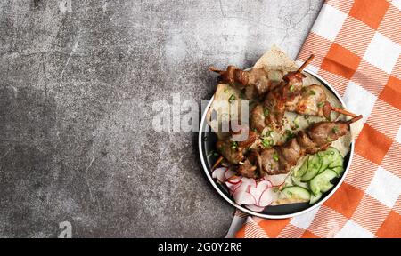 Hähnchenspieße auf dünnem Pita-Brot auf einem runden Teller auf dunkelgrauem Hintergrund. Draufsicht, flach liegend Stockfoto