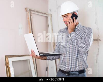 Junge Architektin im Gespräch auf dem Handy mit Laptop in der Hand Stockfoto