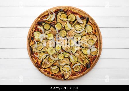 Ganze vegetarische Pizza mit gegrillter Aubergine, Zucchini und Zwiebeln, auf Holzplatte gekrönt. Draufsicht auf Whiteboard-Hintergrund Stockfoto