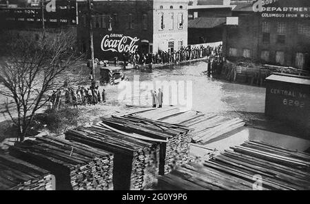 Oldtimer, die durch überflutete Straßen in Columbus, Georgia, fahren, während die Zuschauer von trockenem Boden aus zusehen. Der Chattahoochee River, der an Uptown Columbus entlang fließt, überflutete Mitte Februar 1900 seine Ufer. Stockfoto