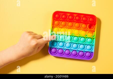 Die Hand eines Kindes drückt auf Pop-it-Spielzeug-Silikon auf einem gelben Hintergrund. Anti-Stress-Spielzeug, ein Trend bei Kinderspielzeug. Stockfoto