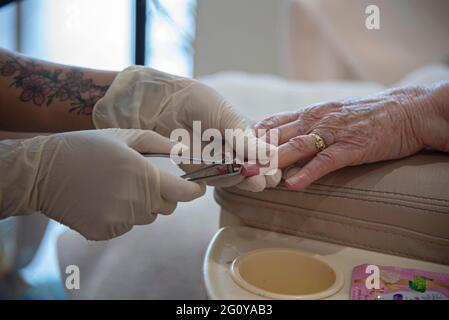 Eine 84-jährige, hispanische Frau, die in ihrem lokalen Schönheitssalon eine Kombination aus Pediküre und Maniküre bekommt. Stockfoto