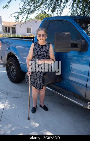 Eine 84-jährige hispanische Frau, die einen Stock in der Hand hält und neben dem Lastwagen ihres Sohnes steht. Stockfoto